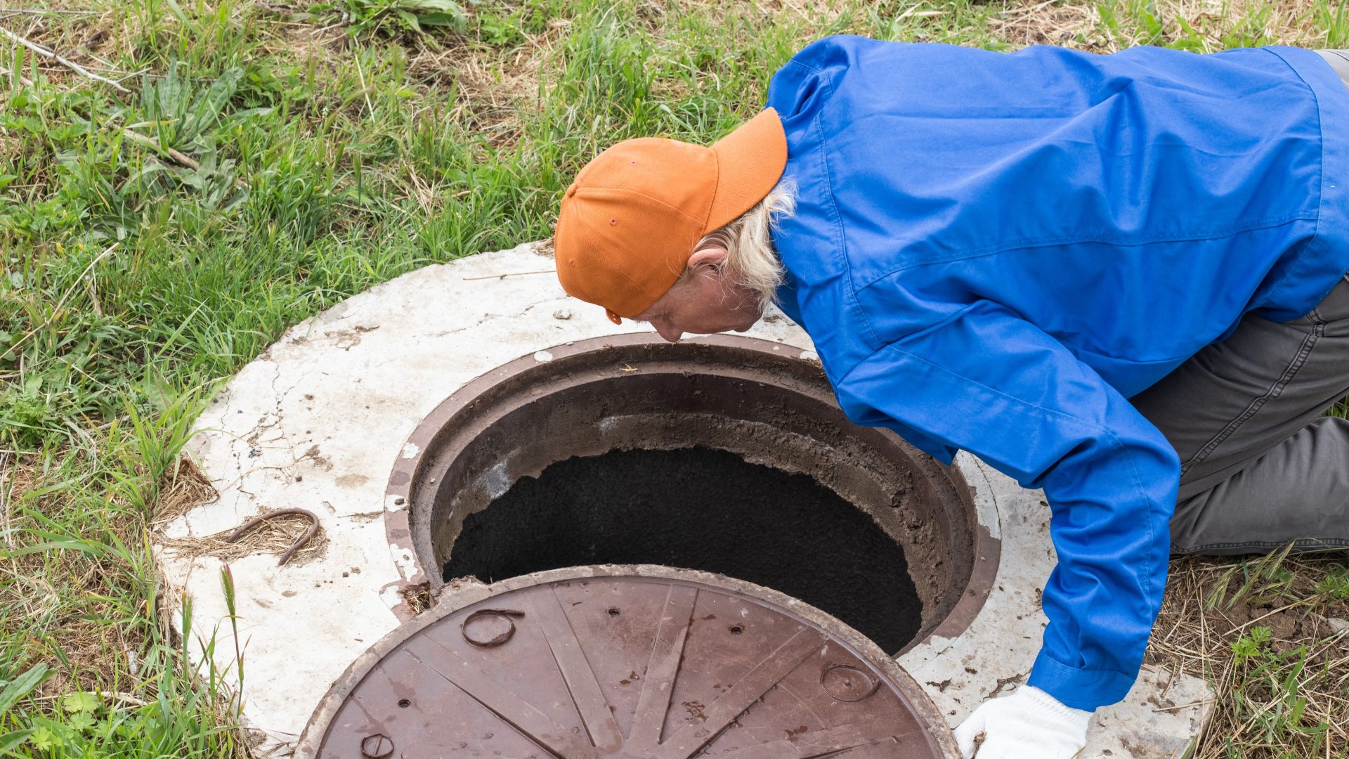 Plumber looking into open septic tank underground