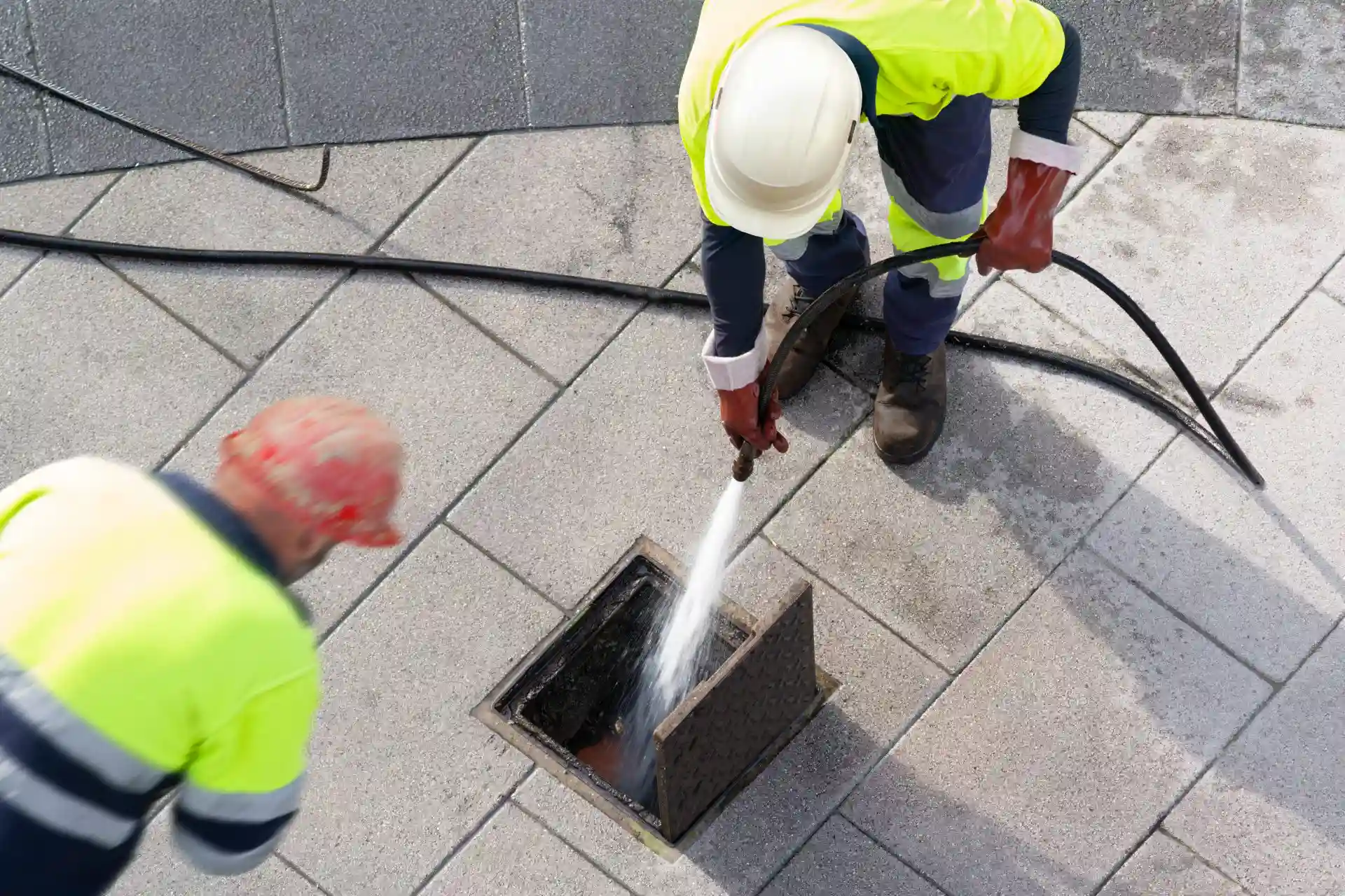 Two Plumbers Cleaning Sewer Drain With Water Jetter