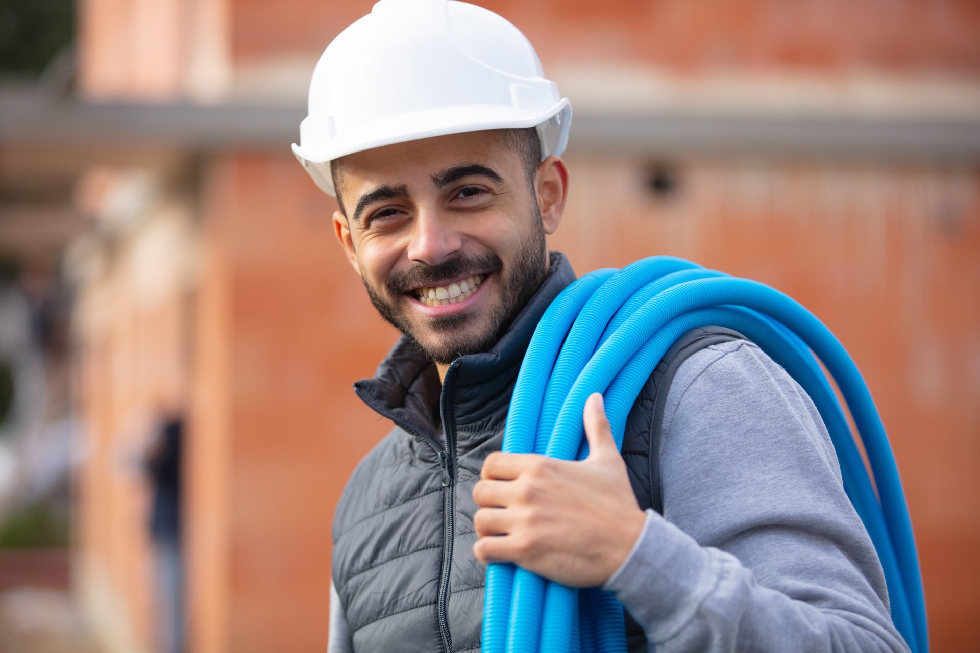 Smiling plumber in white hard hat carrying blue hose
