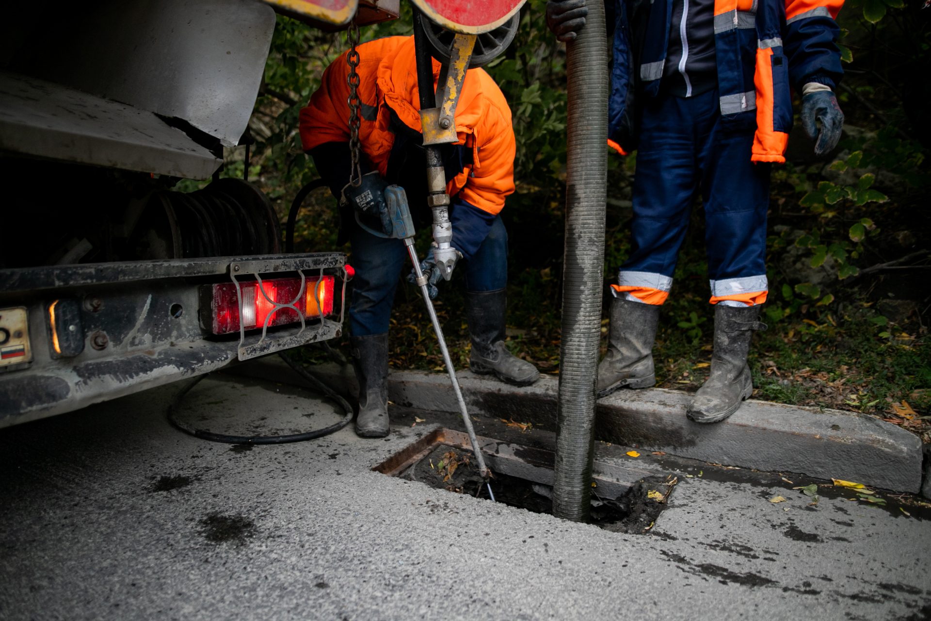 Technicians using hydro jetter to clean out storm drain