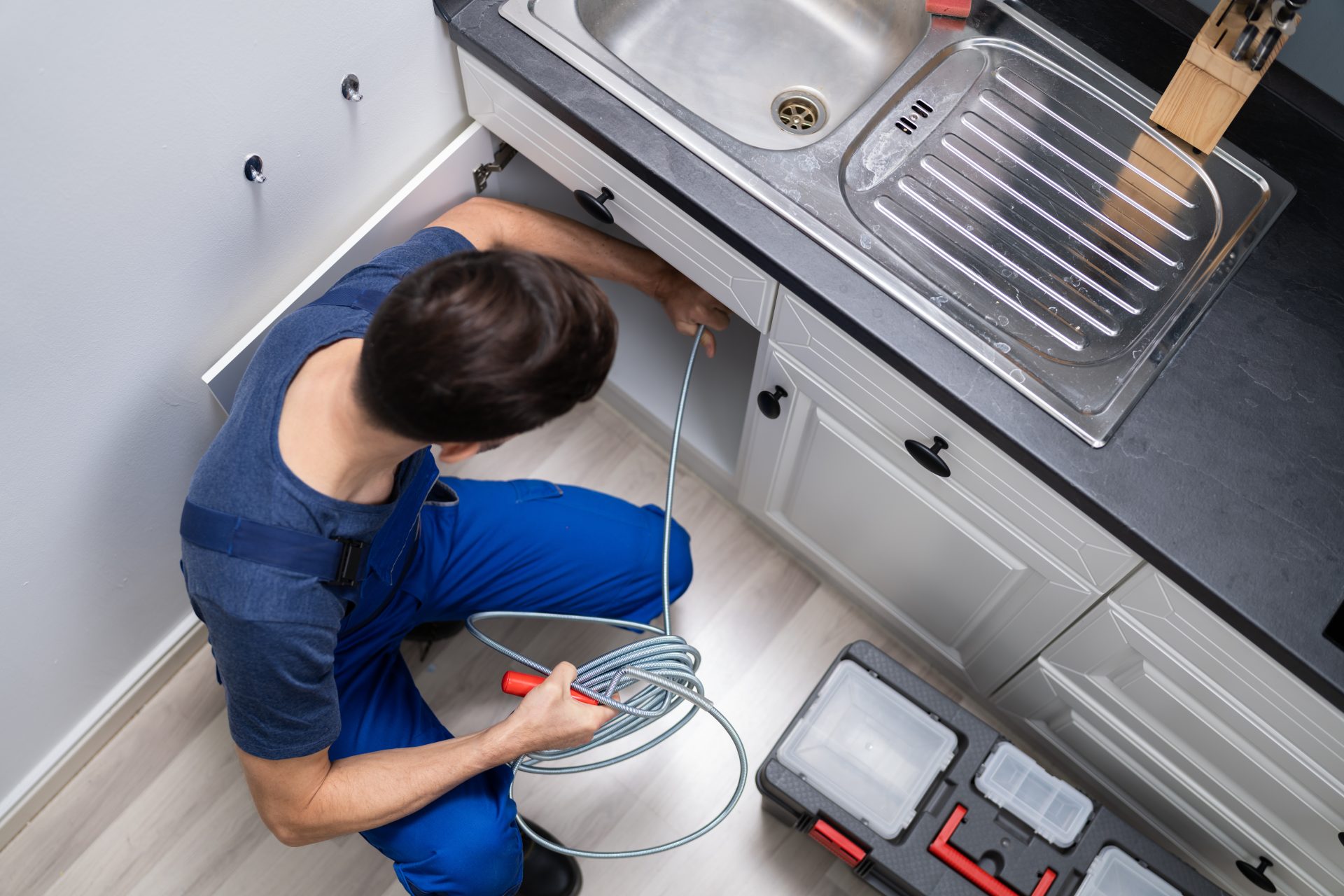 Plumber cleaning clogged kitchen sink pipes