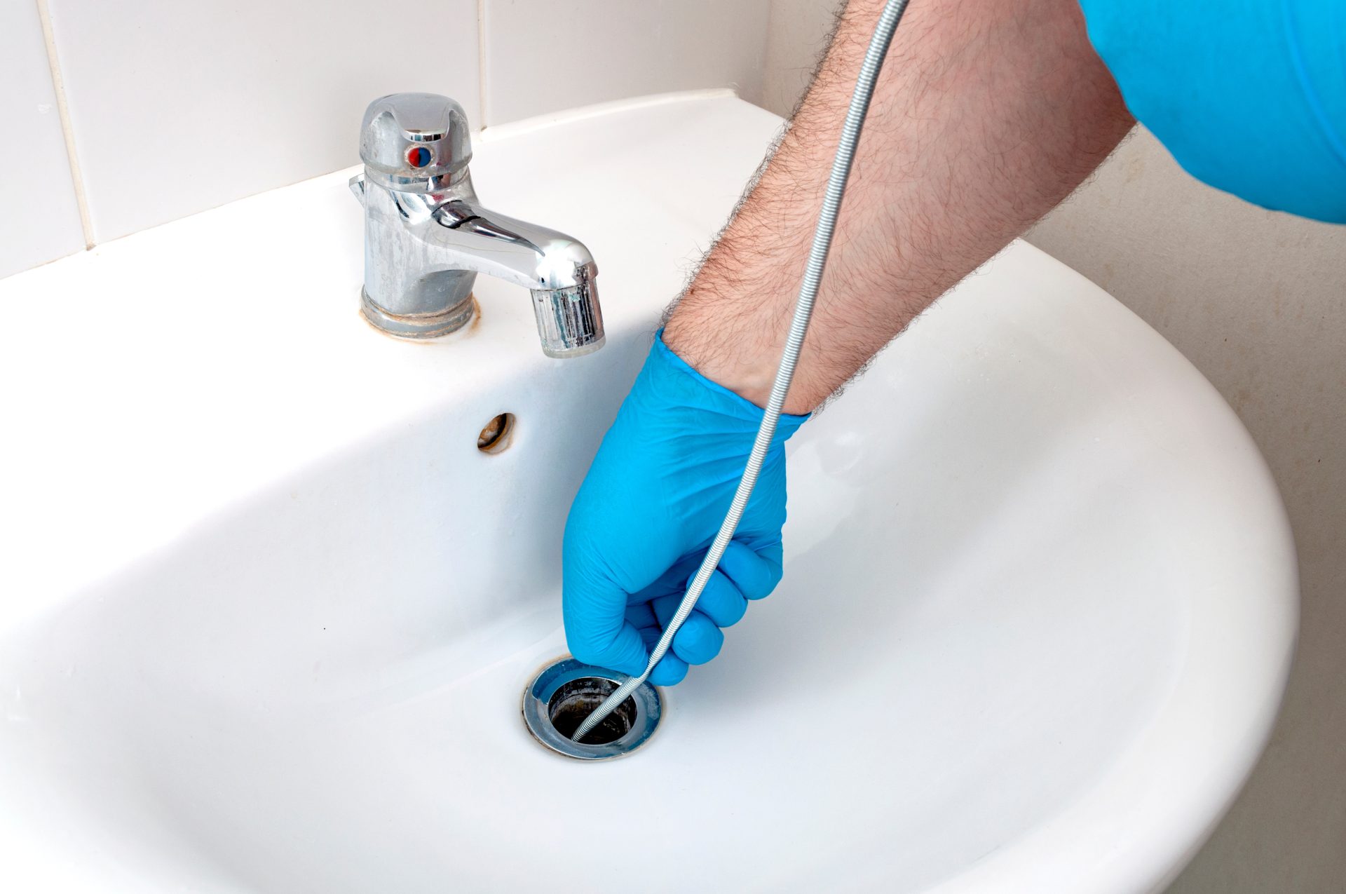 Plumber with blue gloves using drain snake in bathroom sink