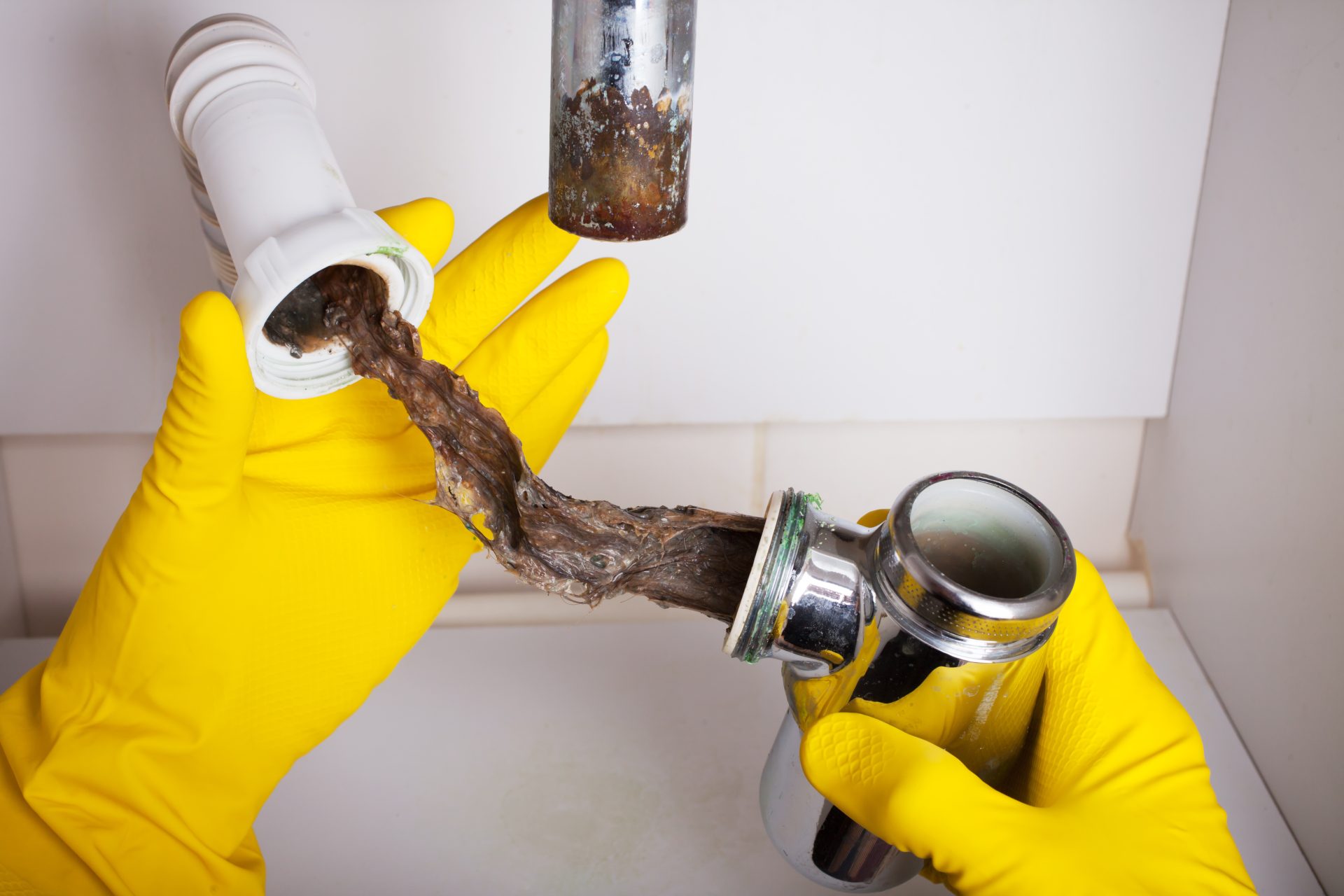 Plumber with gloves revealing significant clog in pipe under sink