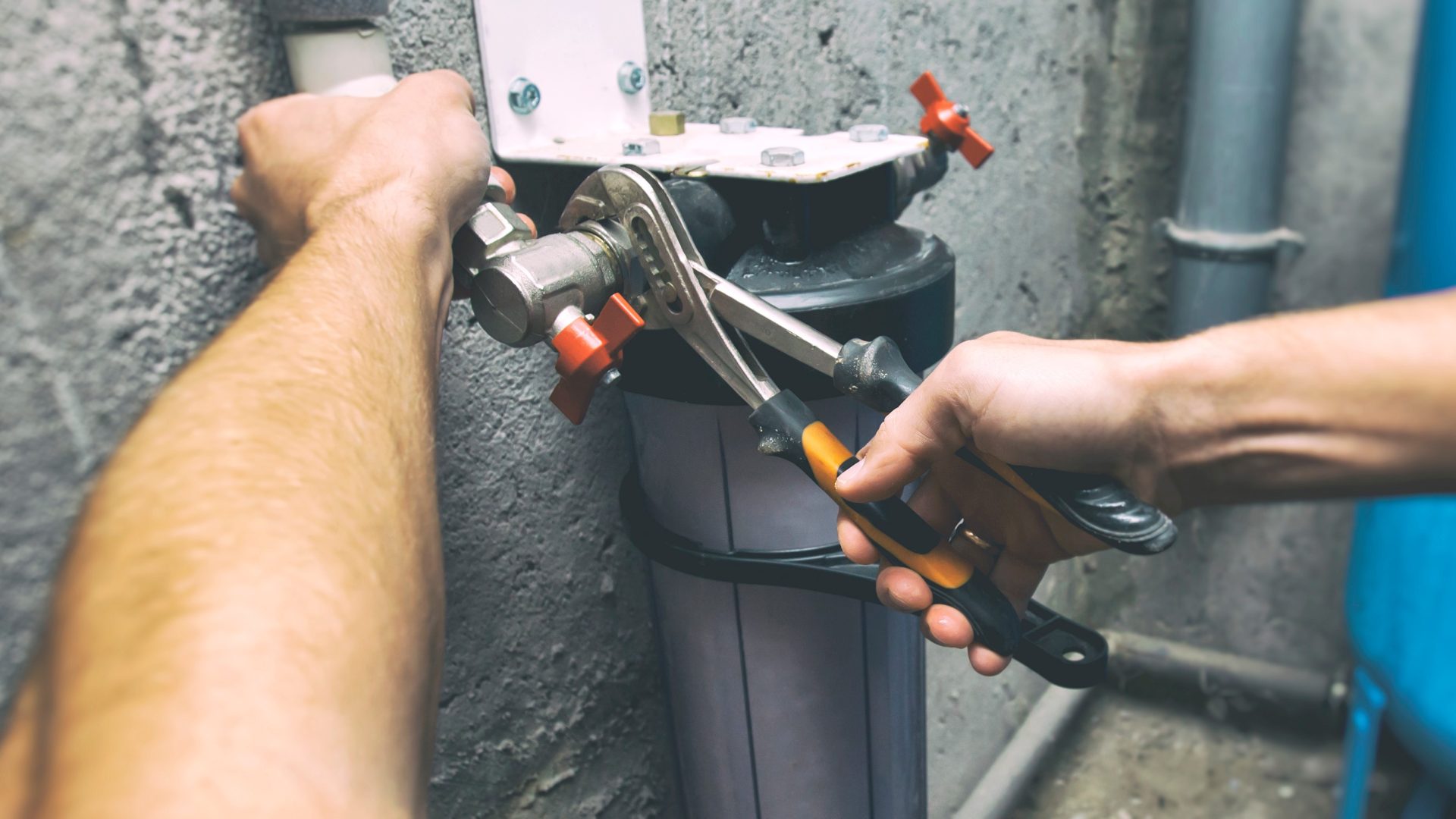 Two hands fixing a water filter with pliers
