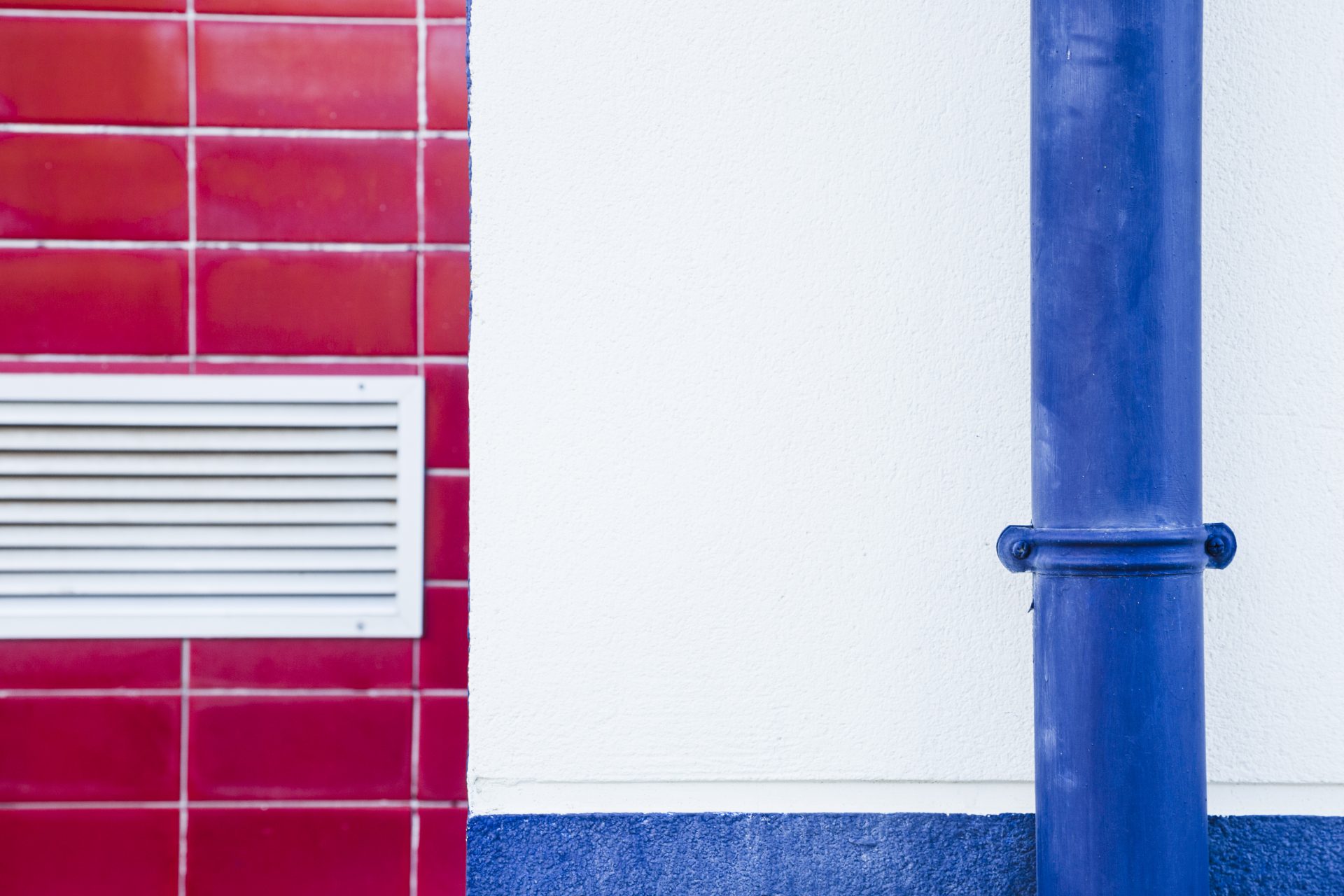 A red tiled wall with a white vent is on the left, and a bright blue gas line pump runs vertically on the right-hand side against a white wall.