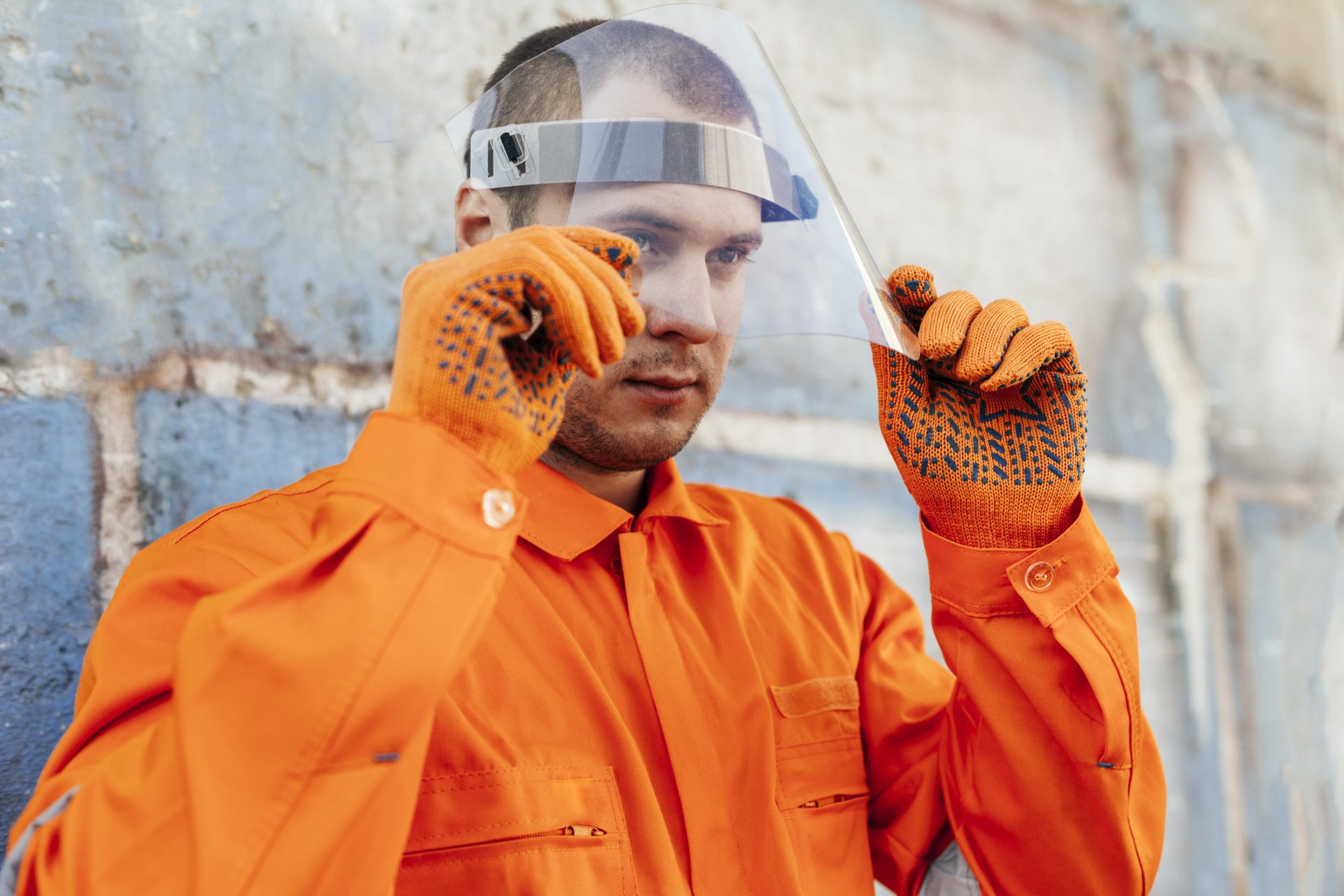 A male sewer inspector wearing an orange uniform and gloves puts on a face guard to protect himself before starting his job.