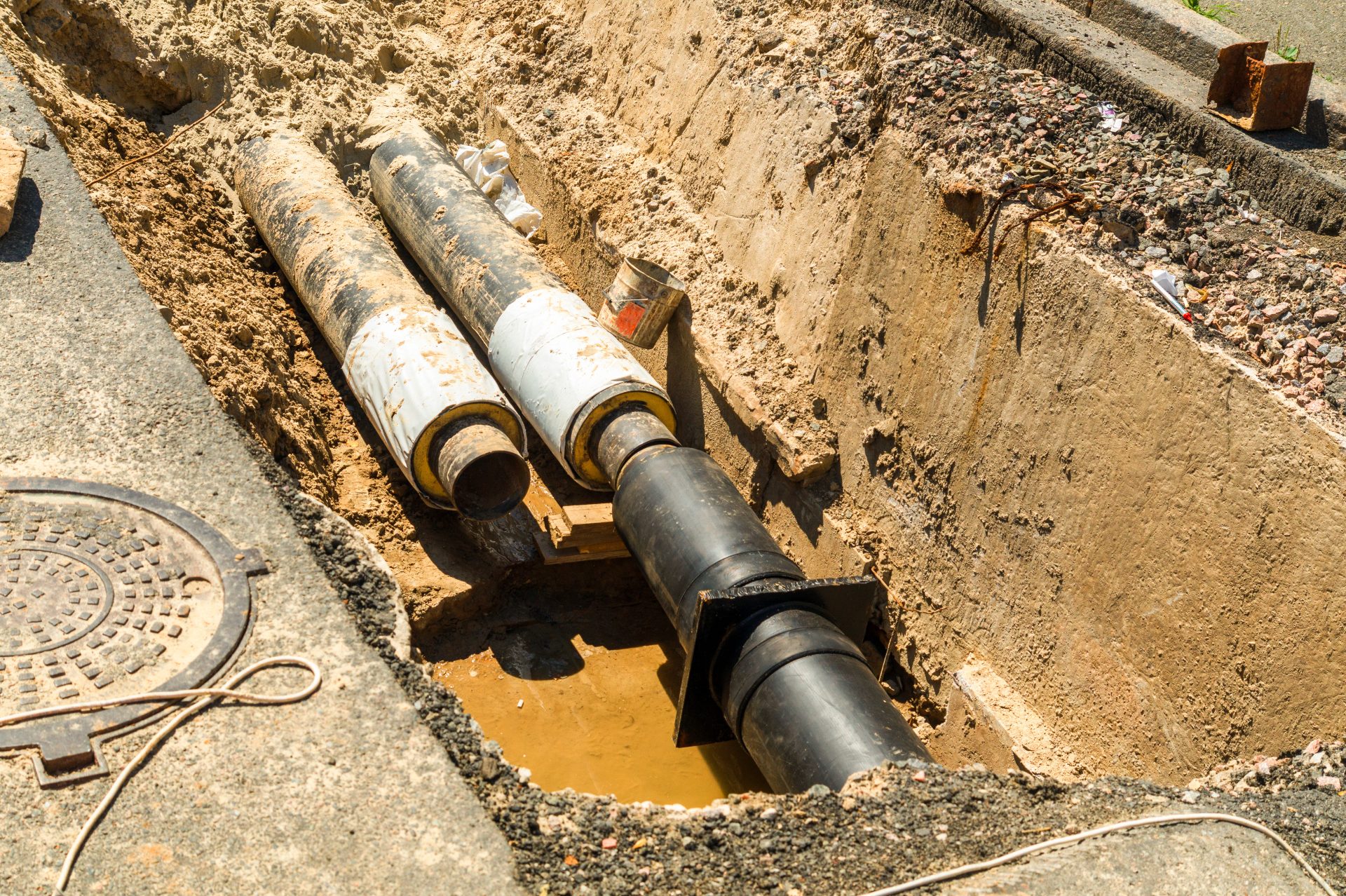 Two exposed underground white and black sewer lines are being installed, with one being further along in the process than the other.
