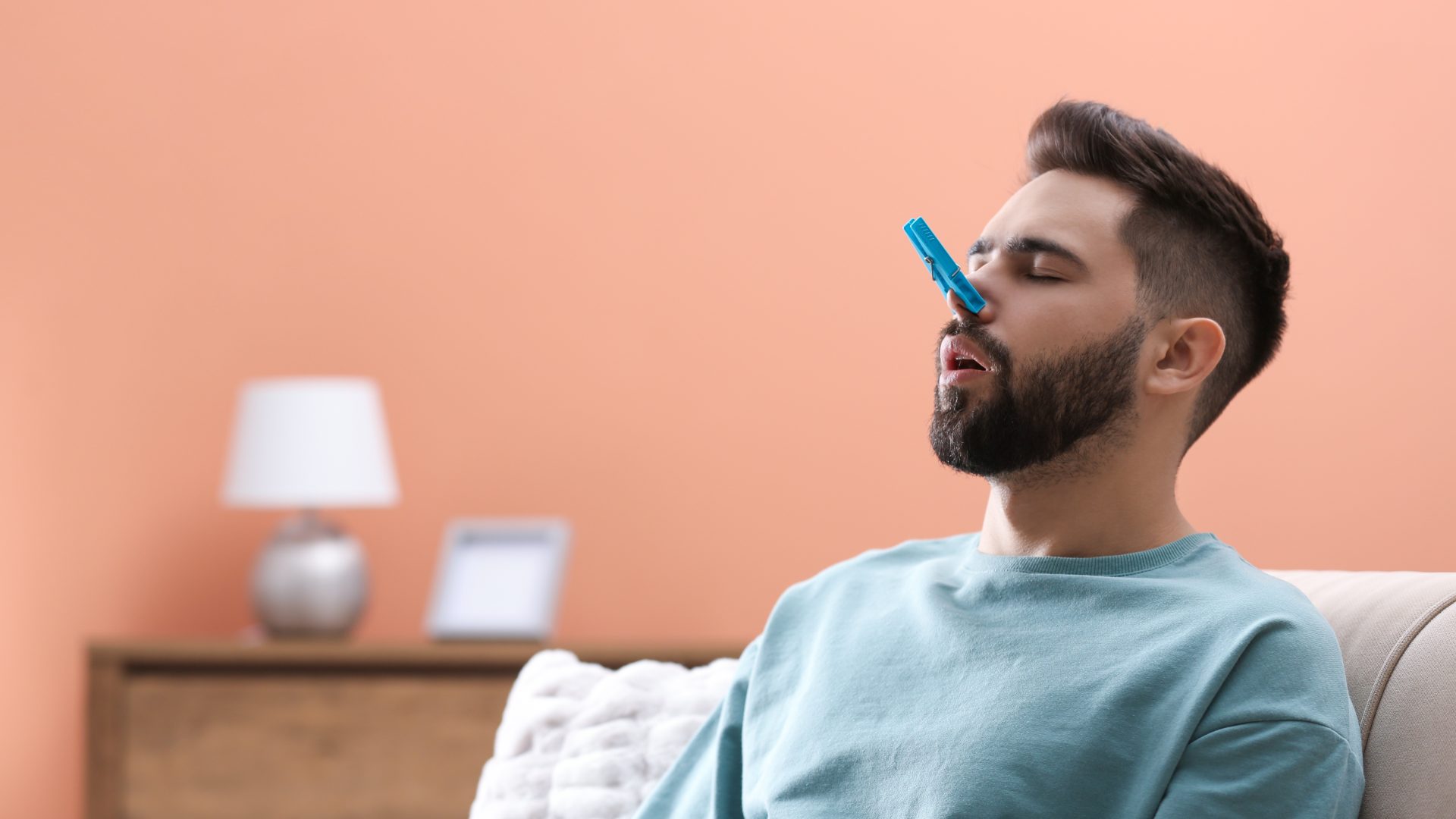 A man sits with a clothespin on his nose to block an unpleasant smell