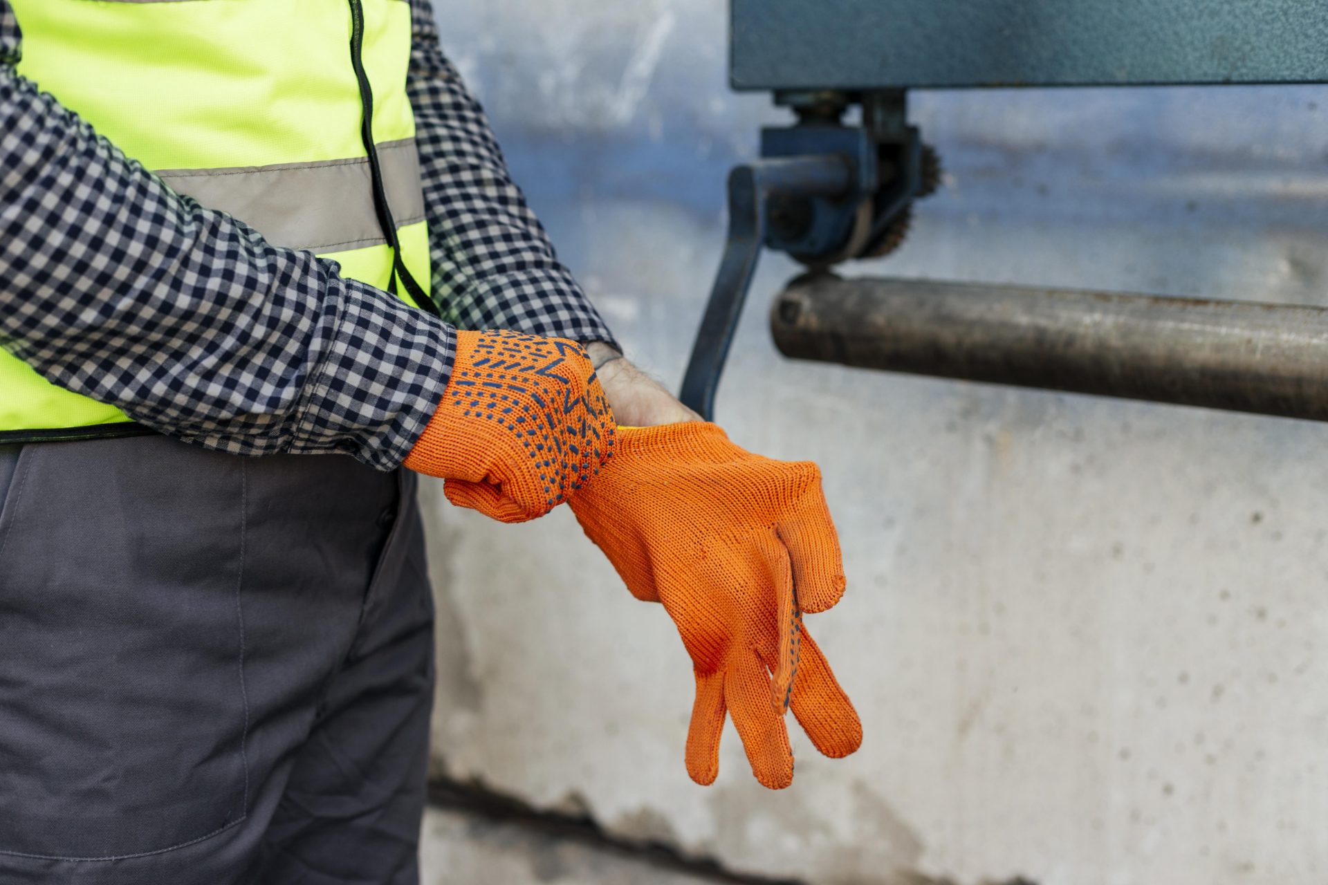 A sewer technician wearing a black and white checkered shirt and grey slacks, putting on bright orange protective gloves before doing a job