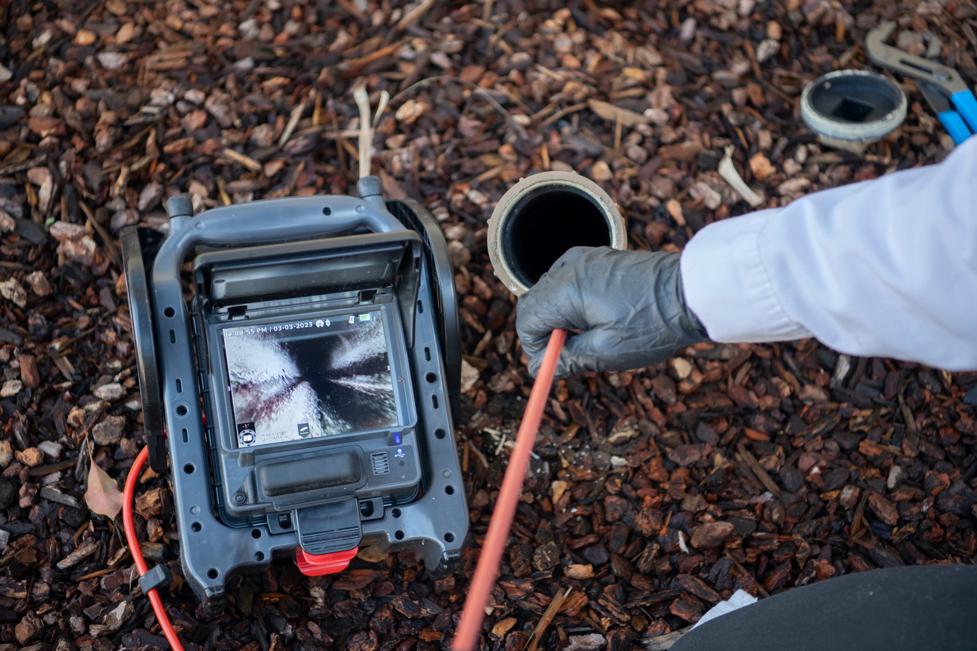 A drain camera next to a sewer line opening showing the inside of the pipe.