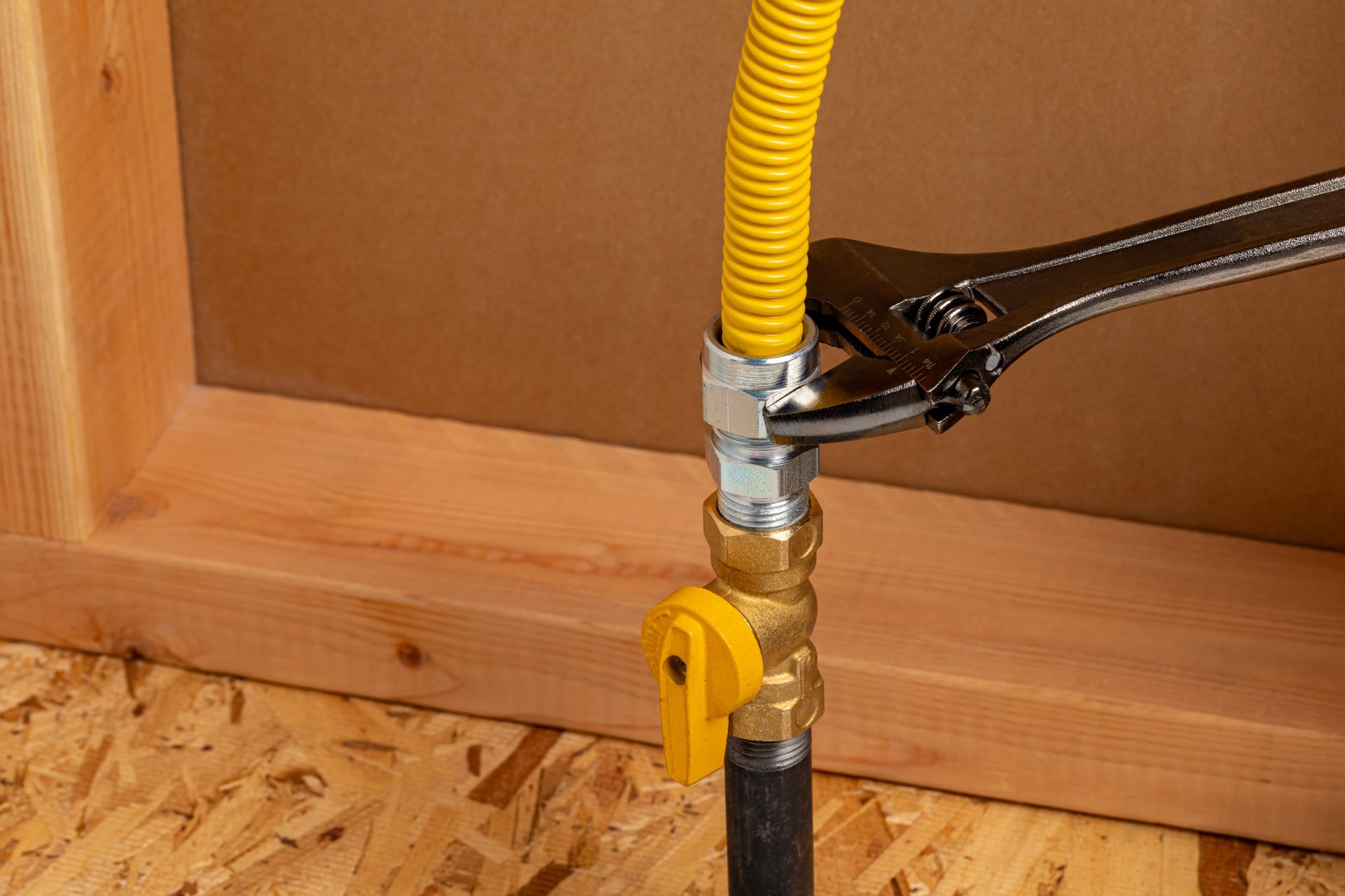 A plumber's hand tightening a newly installed gas line with a wrench.