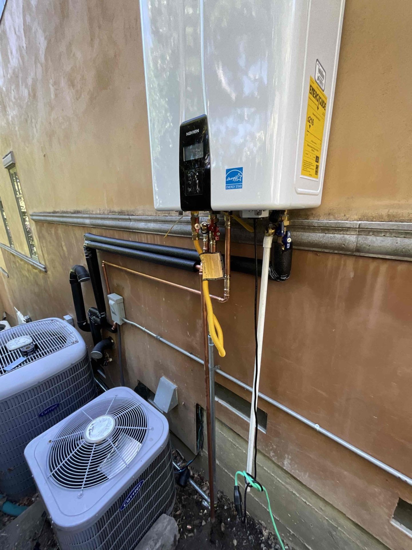 A Navien tankless water heater installed above two AC condensers.
