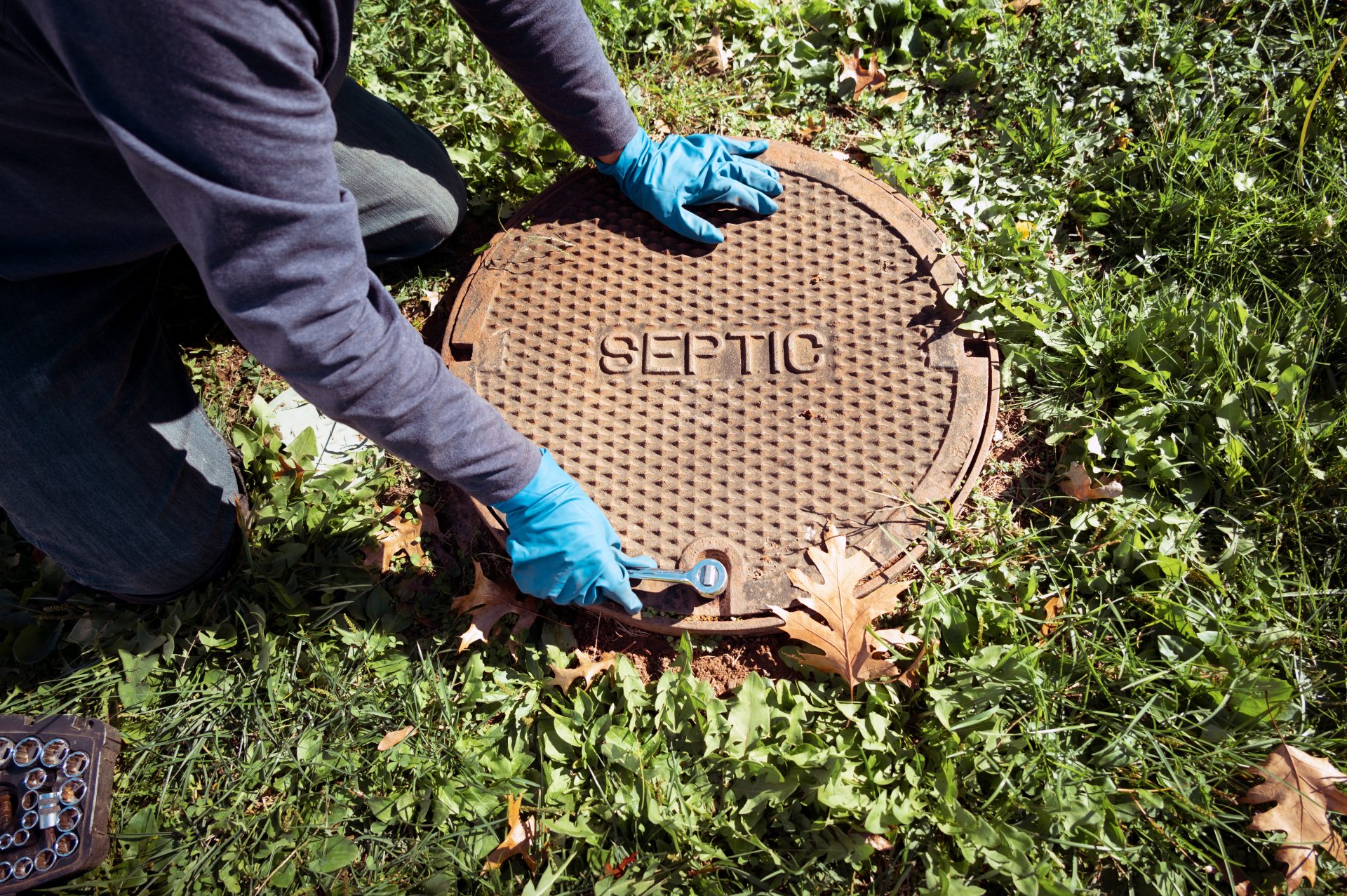 A technician reaches for the cover of a septic tank.