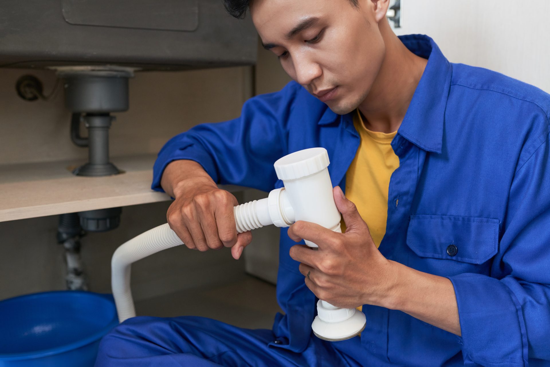 A close-up view of a plumber connecting pipes while working under a sink.