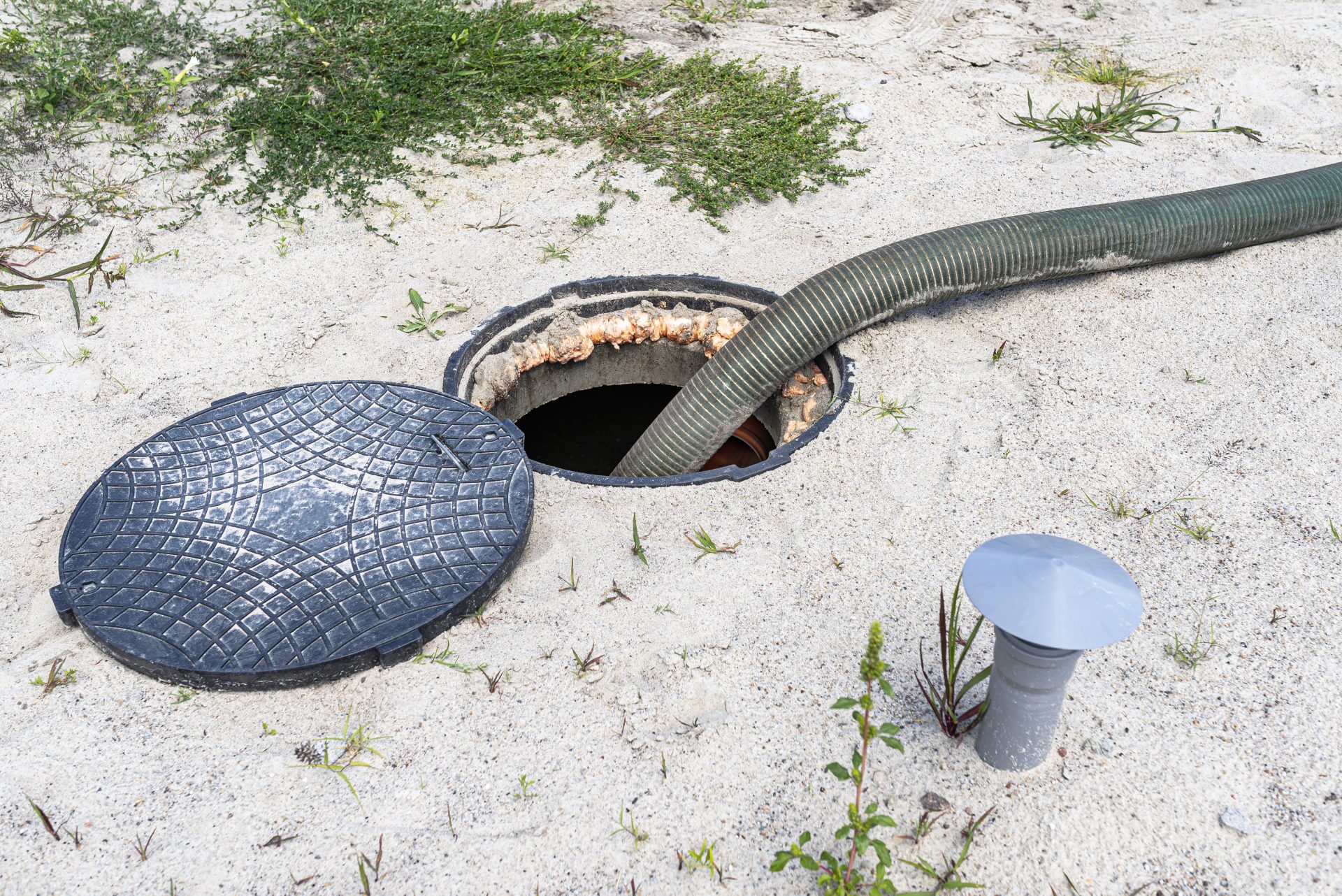 A thin white pipe leaks water from beneath gray connectors. The pipe is partially submerged in muddy water, and the puddle of water is surrounded by more damp dirt.