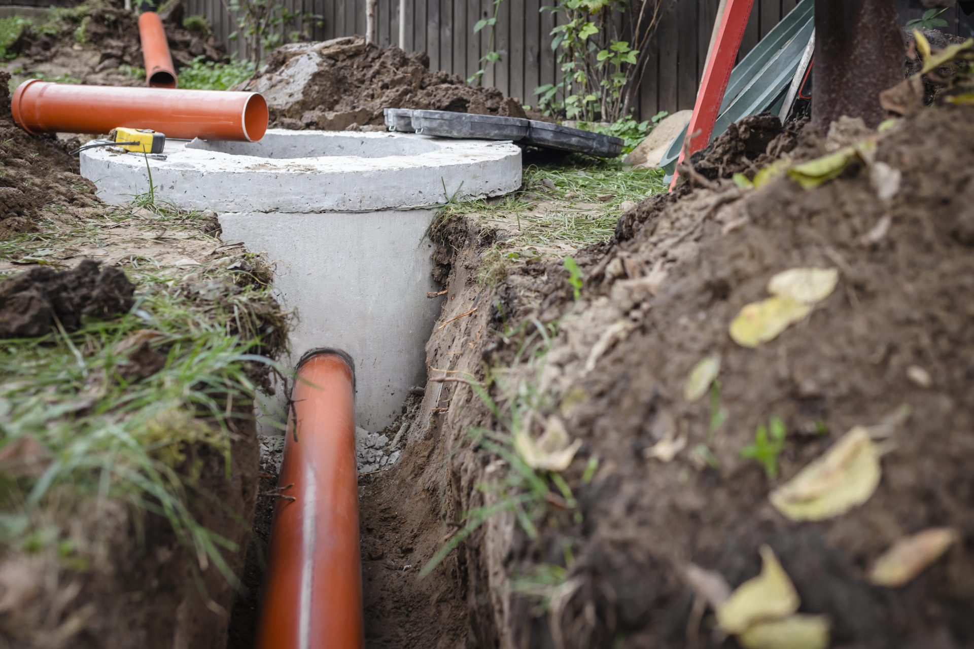 Fancy Plumbing & Rooter Services In East Sonora, CA | Avalon Rooter Part of a septic tank's upper access port is visible during a repair, along with the orange pipes leading from it. The pipes are visible because the dirt has been removed to allow for easier access while work is being done.