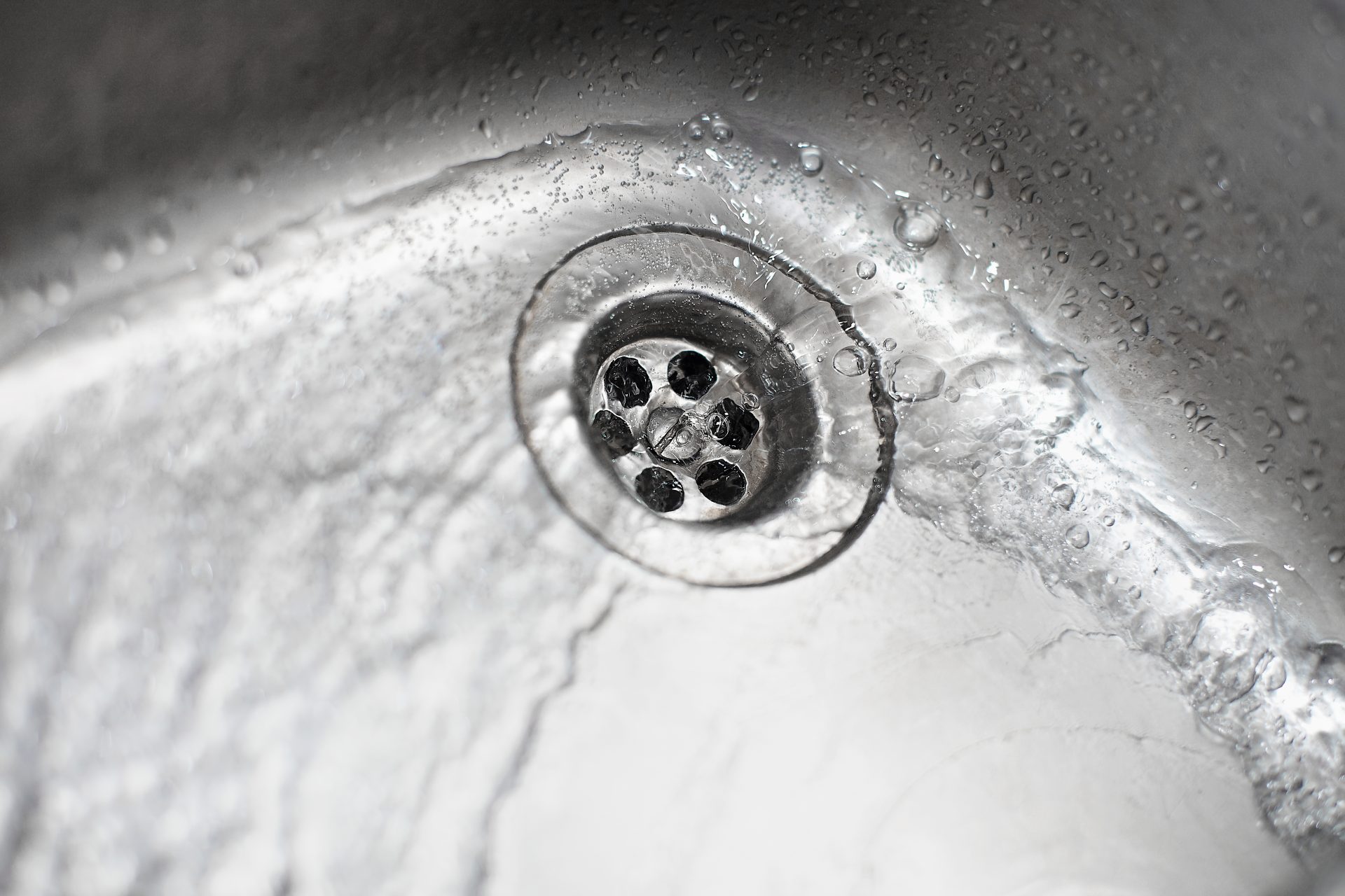 Fabulous Plumbing & Rooter Services In East Sonora, CA | Avalon Rooter A close-up of a stainless steel two-basin sink's tap and handle. Water is flowing from the tap and into the right basin. The backsplash is black and white speckled.