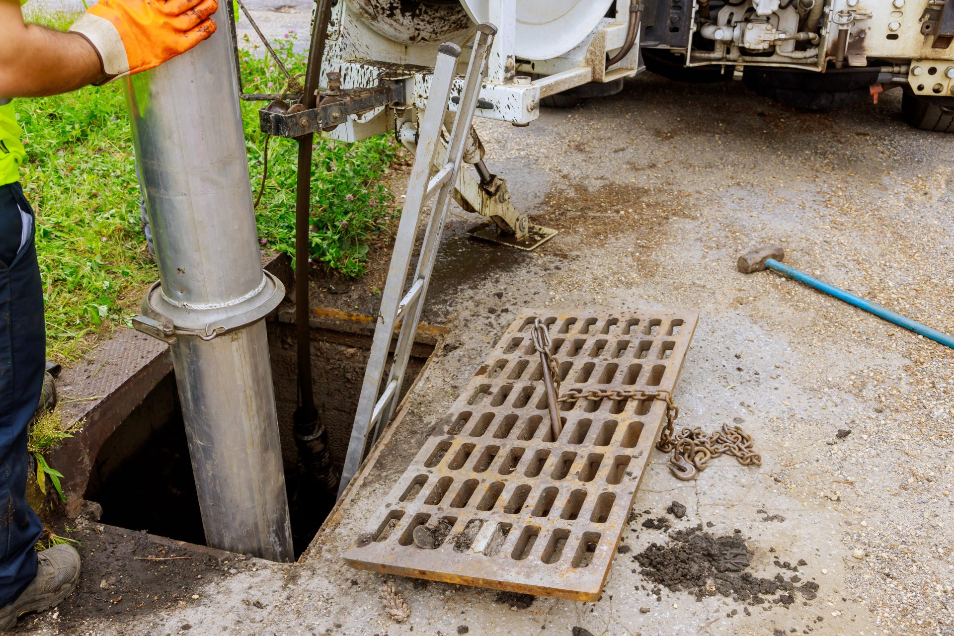 Reliable Sewer Services In East Sonora, CA | Avalon Rooter A person is using a truck and a pump to clean out a sewer pipe. The rectangular grate has been removed, and a silver ladder has been inserted into the opening.
