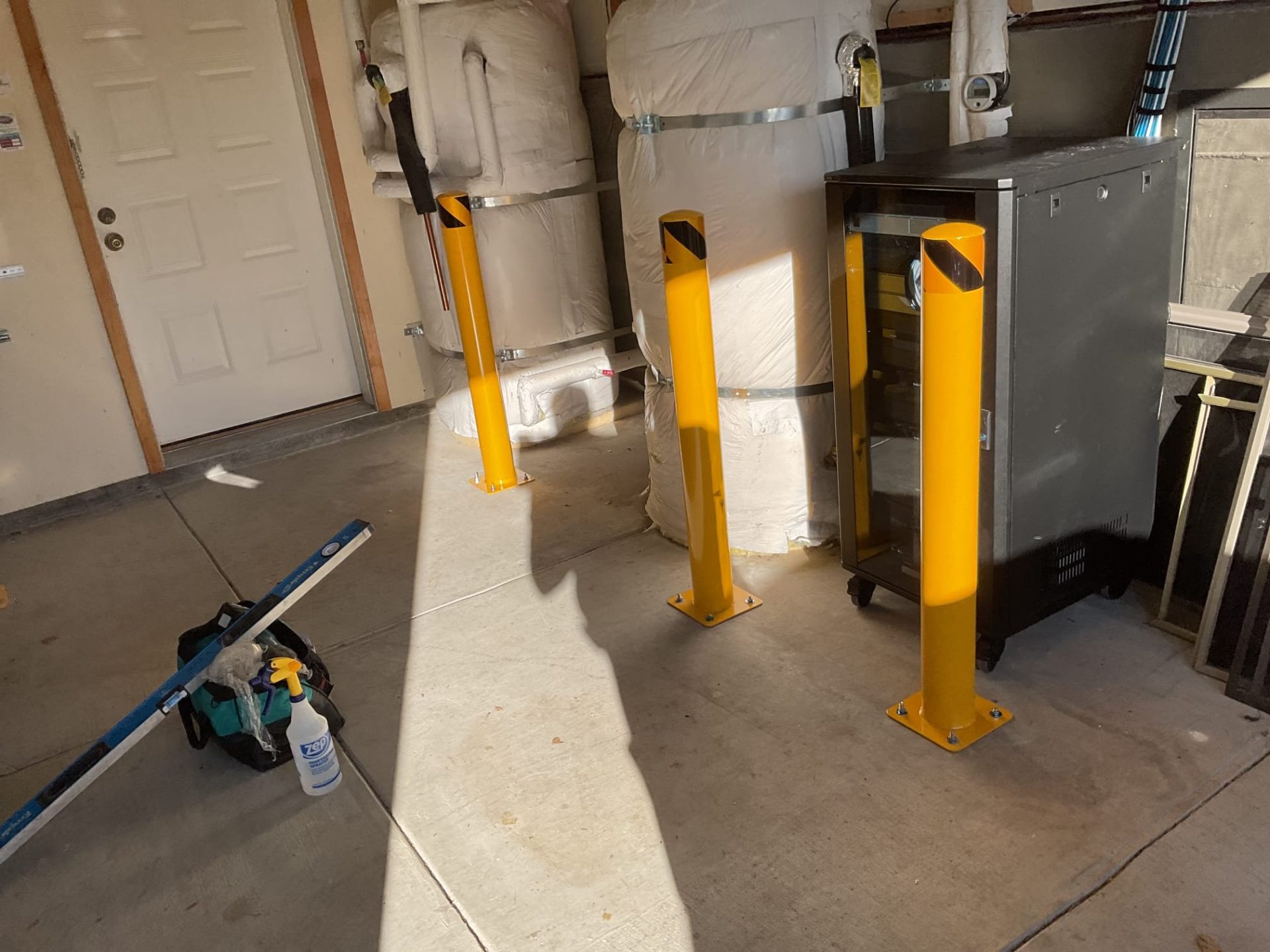 Yellow safety bollards are installed in a garage alongside utility equipment as part of professional plumbing & rooter services.
