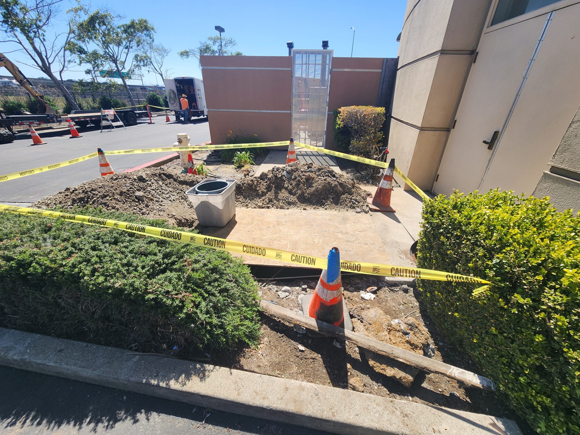An outdoor work zone secured with caution tape and safety cones marks an active excavation site for commercial plumbing & rooter services.