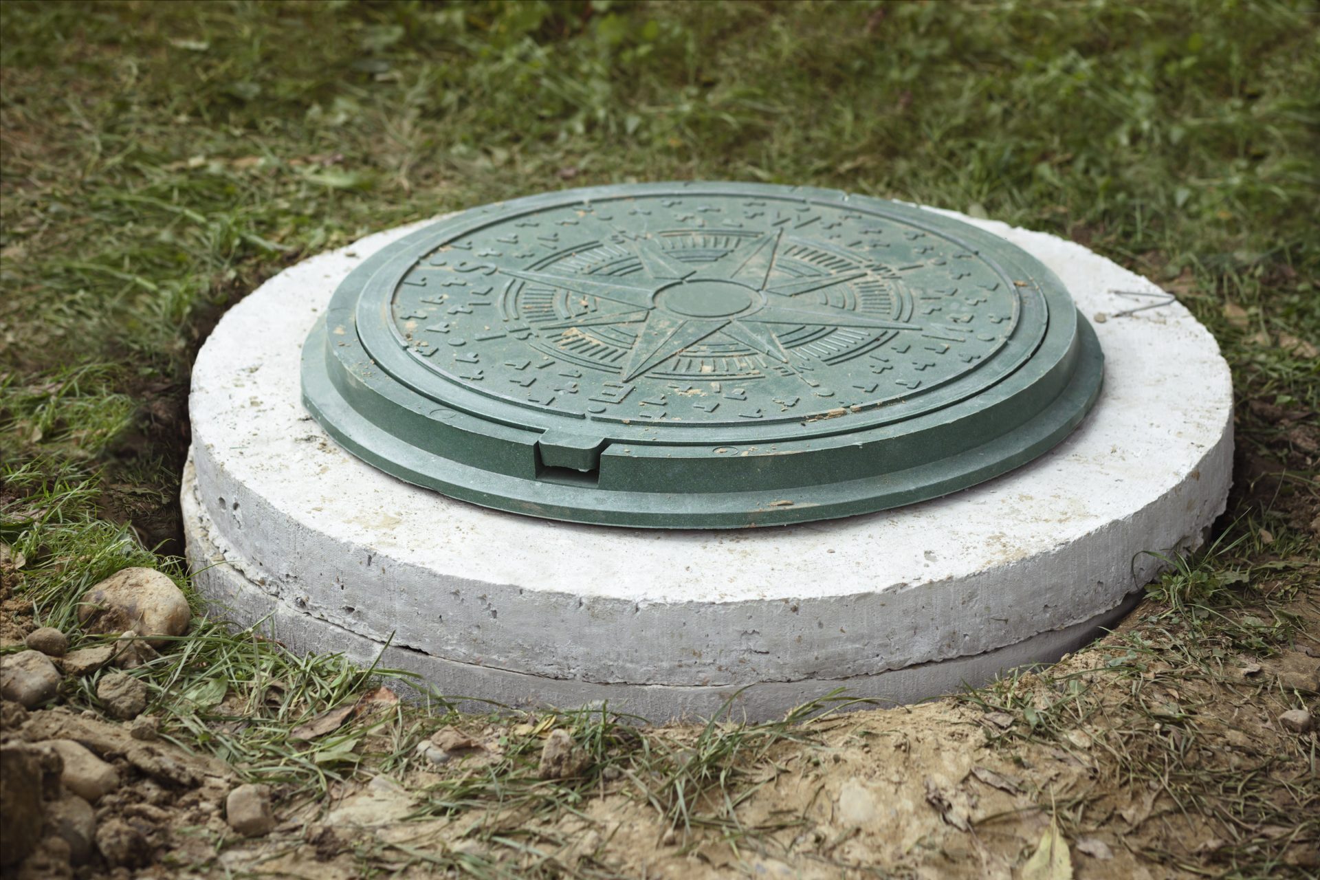 A green decorative riser lid sits securely atop a concrete access riser installed during a Septic Tank Replacement project.