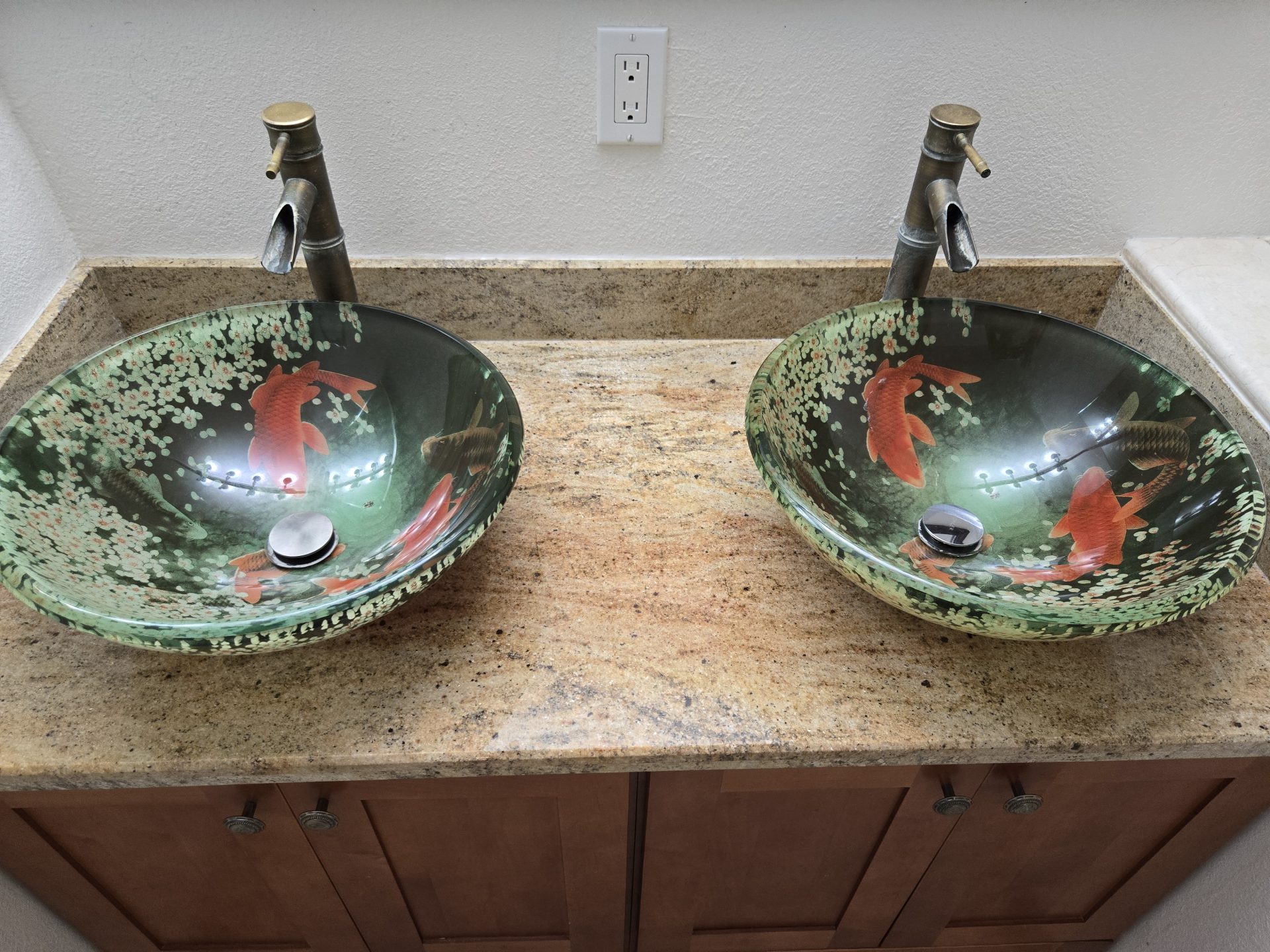 Two decorative glass vessel sinks with fish designs sit on a granite countertop as part of professional plumbing & rooter services.