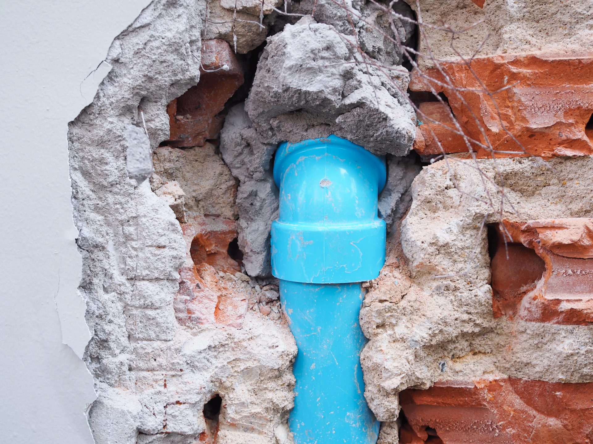 A blue PVC elbow pipe is embedded within a damaged masonry wall during a Septic Tank Replacement project.
